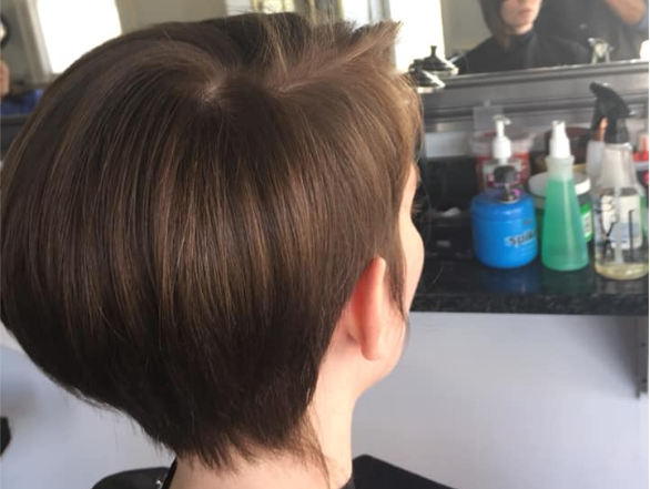 Short brown haircut viewed from behind in a salon mirror, with a mirror and hair products visible ahead