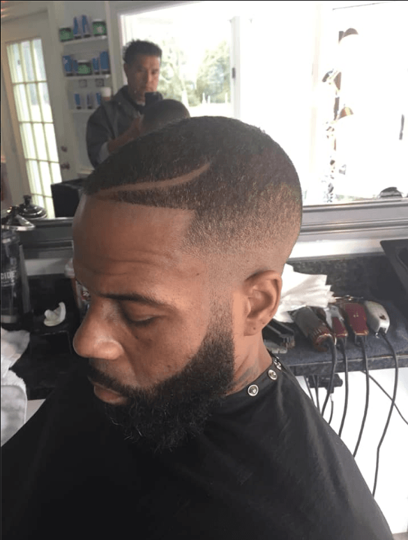 Close-up of a man with a fresh fade haircut in a barbershop chair, mirror and styling tools behind him.