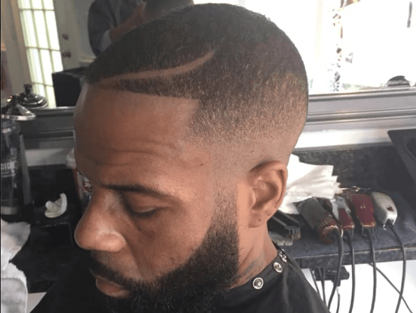 Side profile of a man with a beard and fade haircut in a barbershop chair.