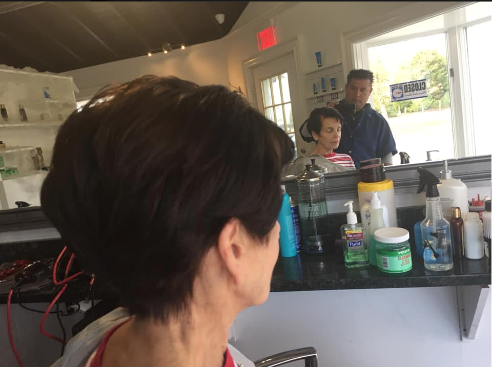 Person with short dark hair seen from behind in a salon, facing a mirror and counter with products.