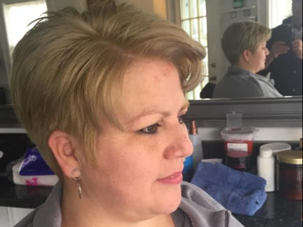 Woman with short blonde hair in profile, seated indoors beside a mirror and salon-style counter.