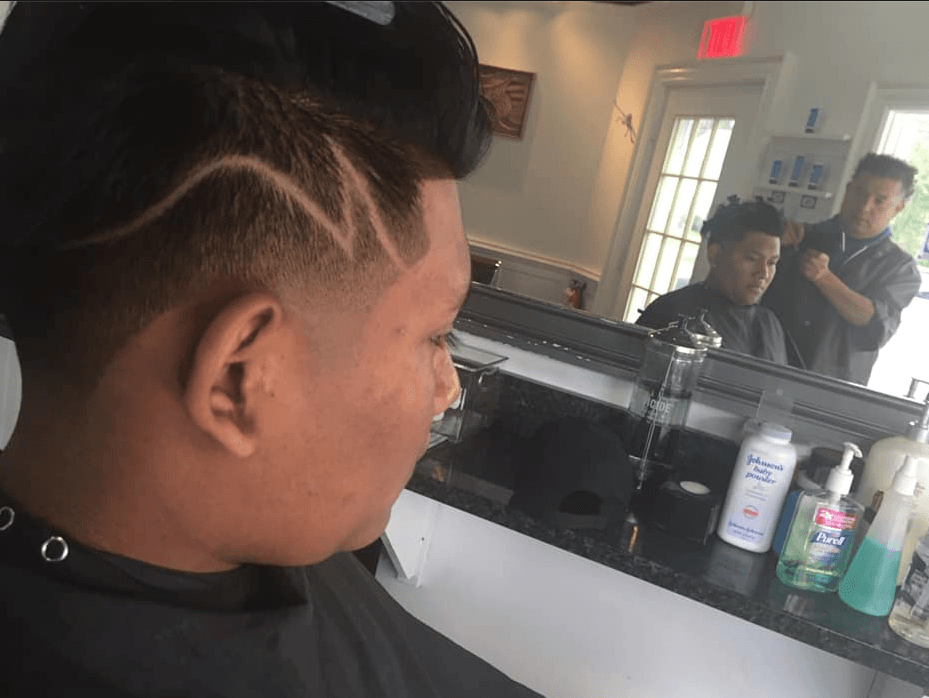 Person with braided hair getting a haircut in a salon mirror view, with styling products on the counter.
