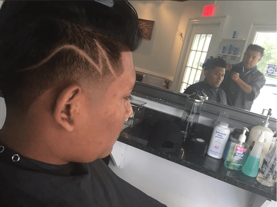 Barber trimming a client’s hair in a salon mirror view, with hair products on the counter.