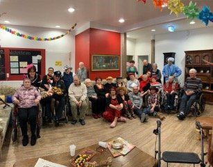 Gruppe von Menschen in einem dekorierten Raum, einige in Kostümen. Einige benutzen Rollstühle. Partystimmung.
