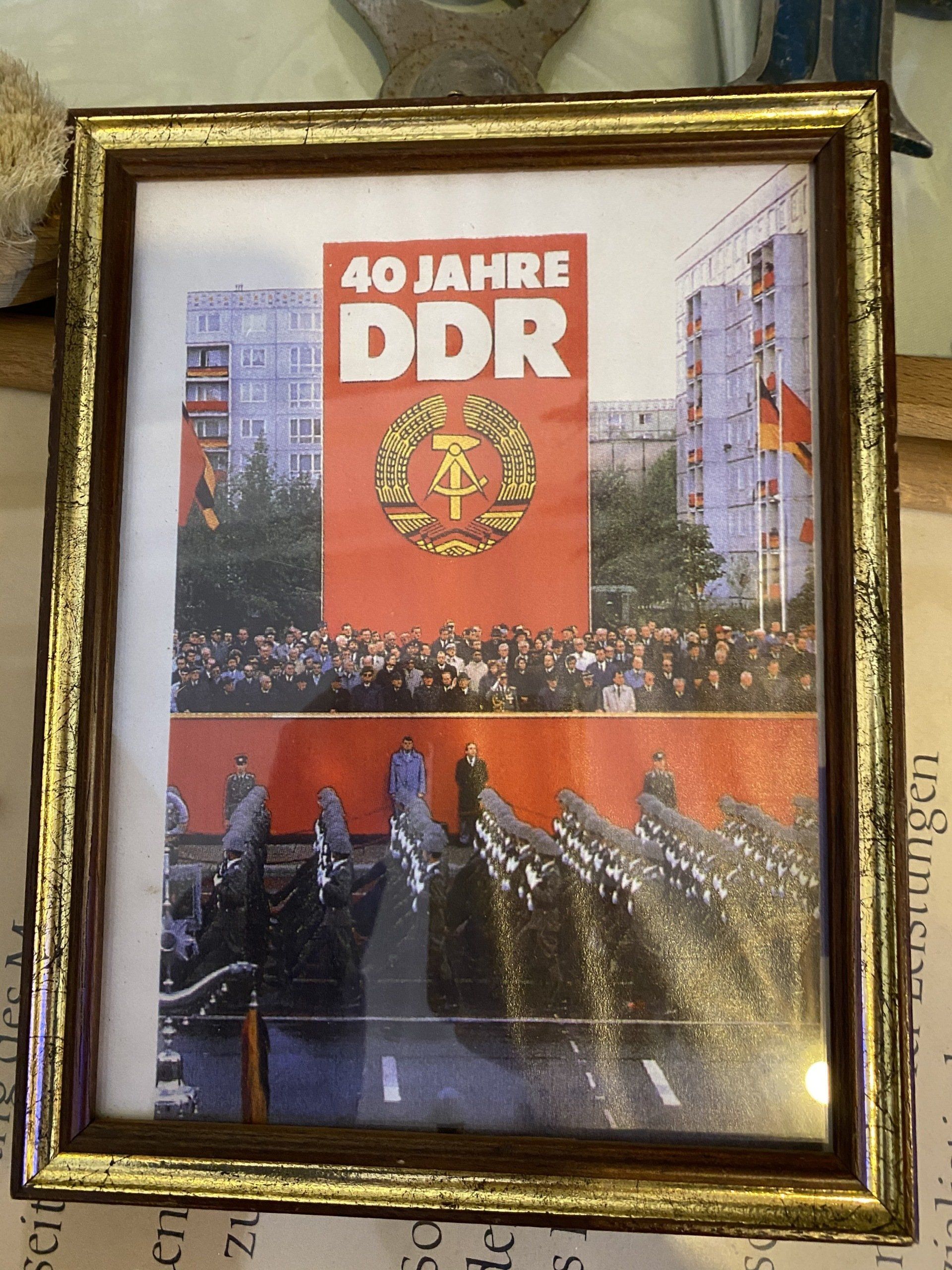 Gerahmtes Foto: Ostdeutsche Parade zum 40-jährigen Jubiläum der DDR. Militärmarsch, rotes Banner, Text „40 JAHRE DDR“.