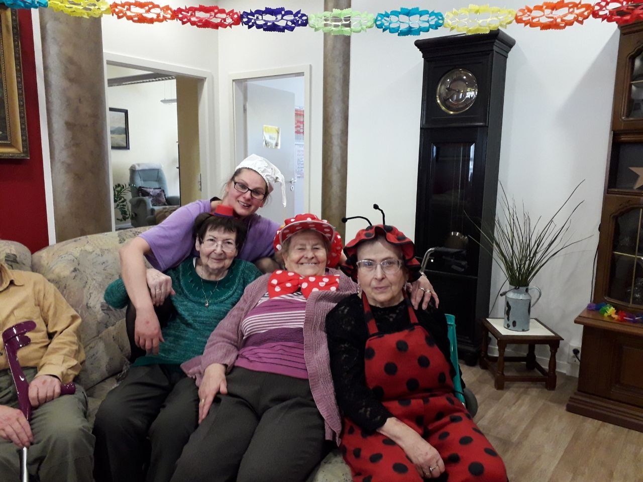 Gruppe von Menschen in Kostümen sitzt auf einem Sofa. Eine Person trägt ein Marienkäferkostüm, andere tragen Hüte. 