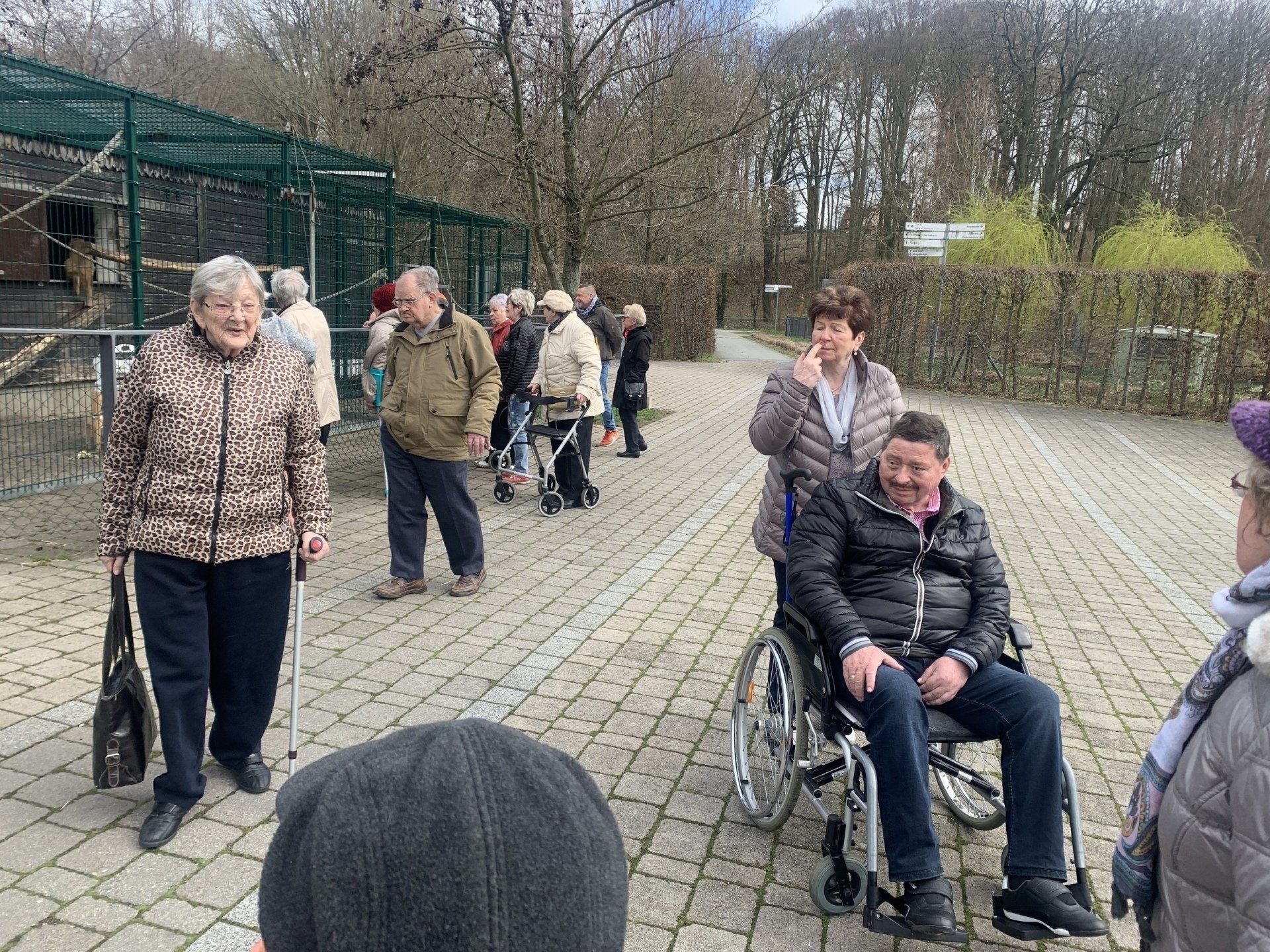 Gruppe von Menschen, darunter jemand im Rollstuhl, draußen in der Nähe eines Gebäudes und von Bäumen.