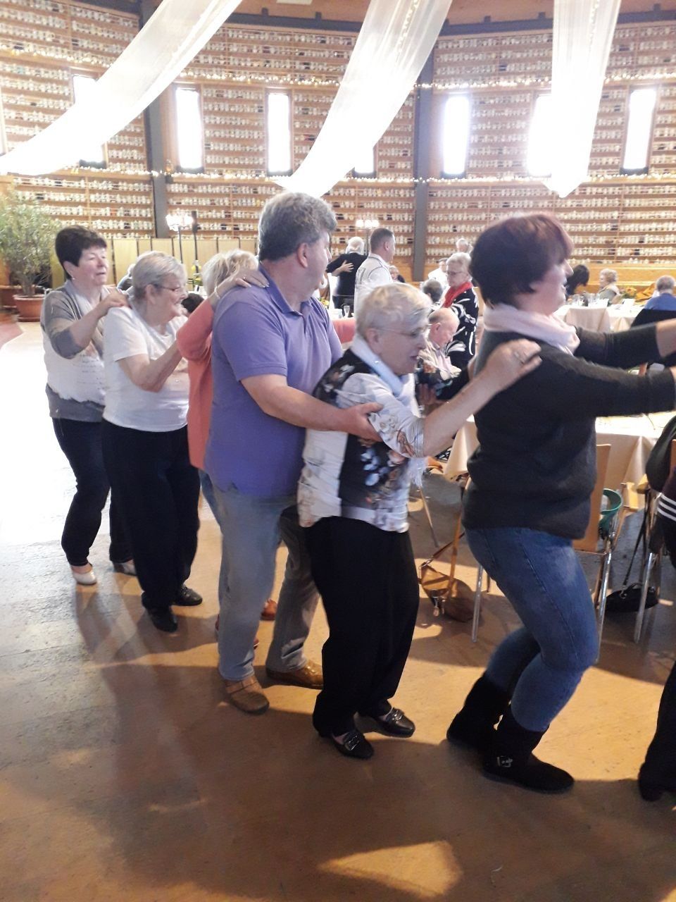 Menschen tanzen in einer Polonaise. Drinnen. Manche halten sich gegenseitig an den Schultern.