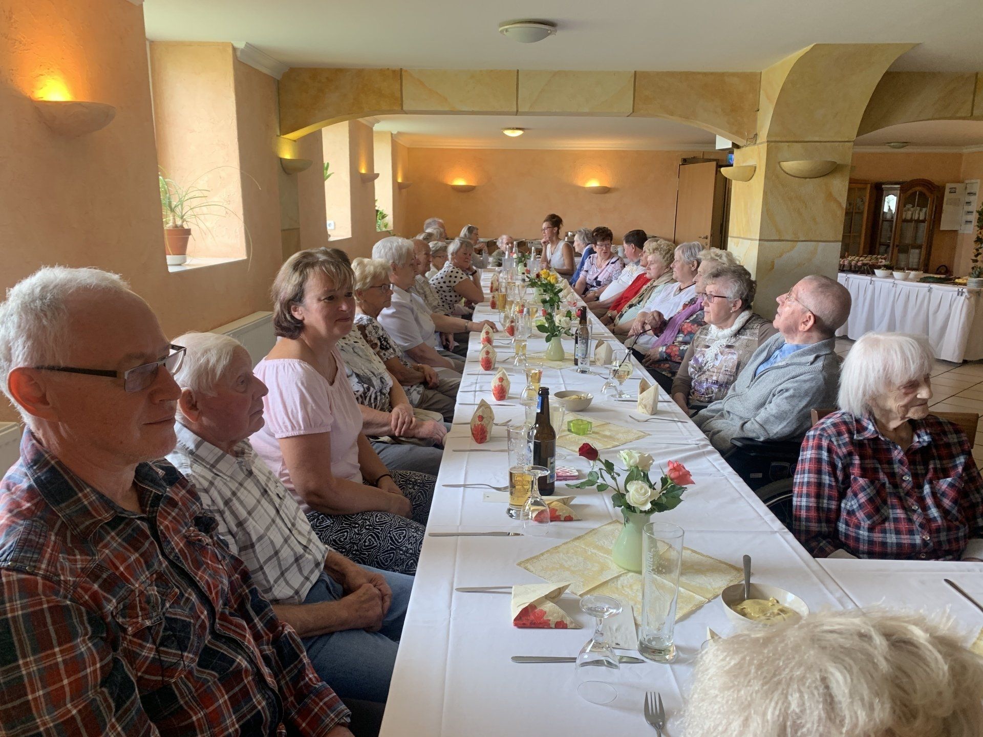Menschen sitzen an einem langen Tisch, wahrscheinlich bei einer Veranstaltung oder einem Essen. 