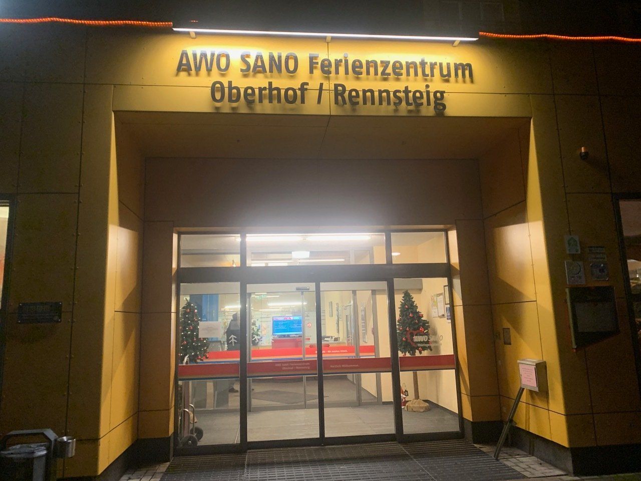 Eingang zum AWO SANO Ferienzentrum Oberhof/Brennsteig, mit Leuchtschild über den Glastüren.
