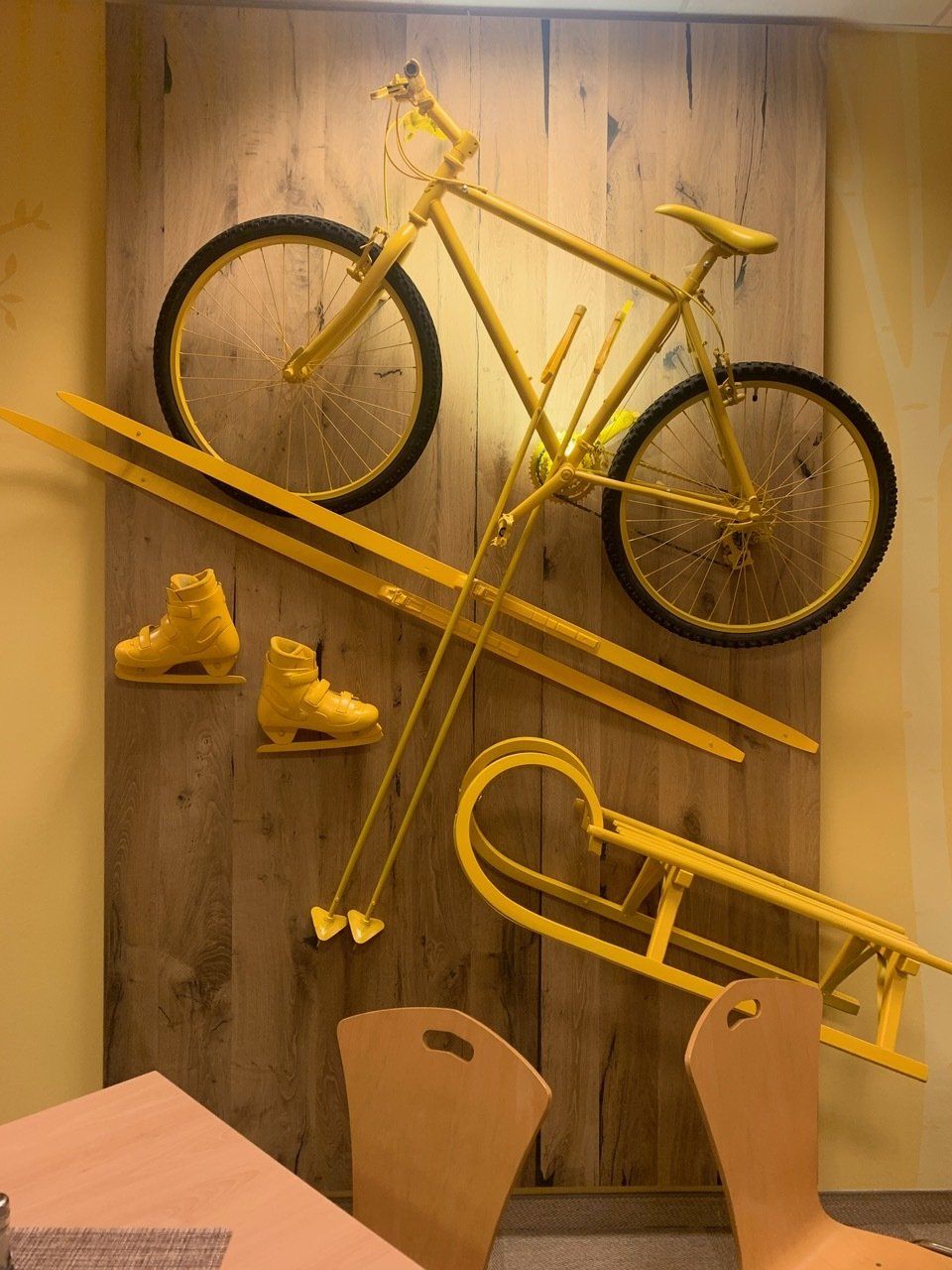 Gelbes Fahrrad, Skier, Schlittschuhe und Schlitten an einer Holzwand.