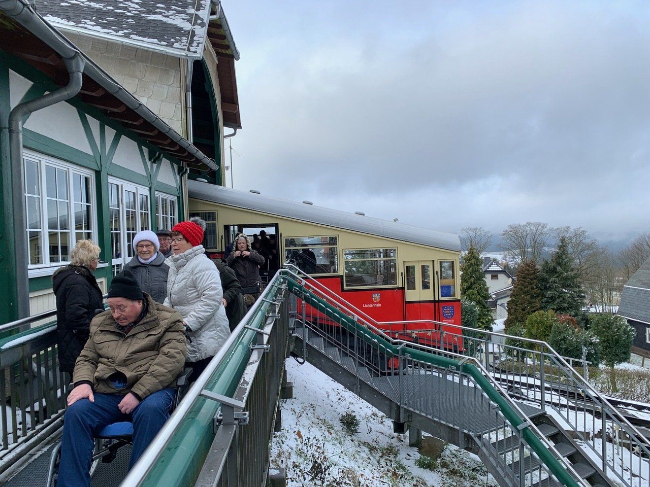 Menschen steigen an einem verschneiten Tag in eine rote Standseilbahn. Eine Person im Rollstuhl wartet.