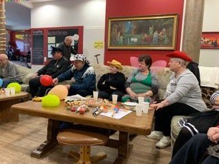 Eine Gruppe von Menschen in Kostümen sitzt auf einem Sofa. Vor ihnen steht ein Tisch mit Essen und Luftballons.