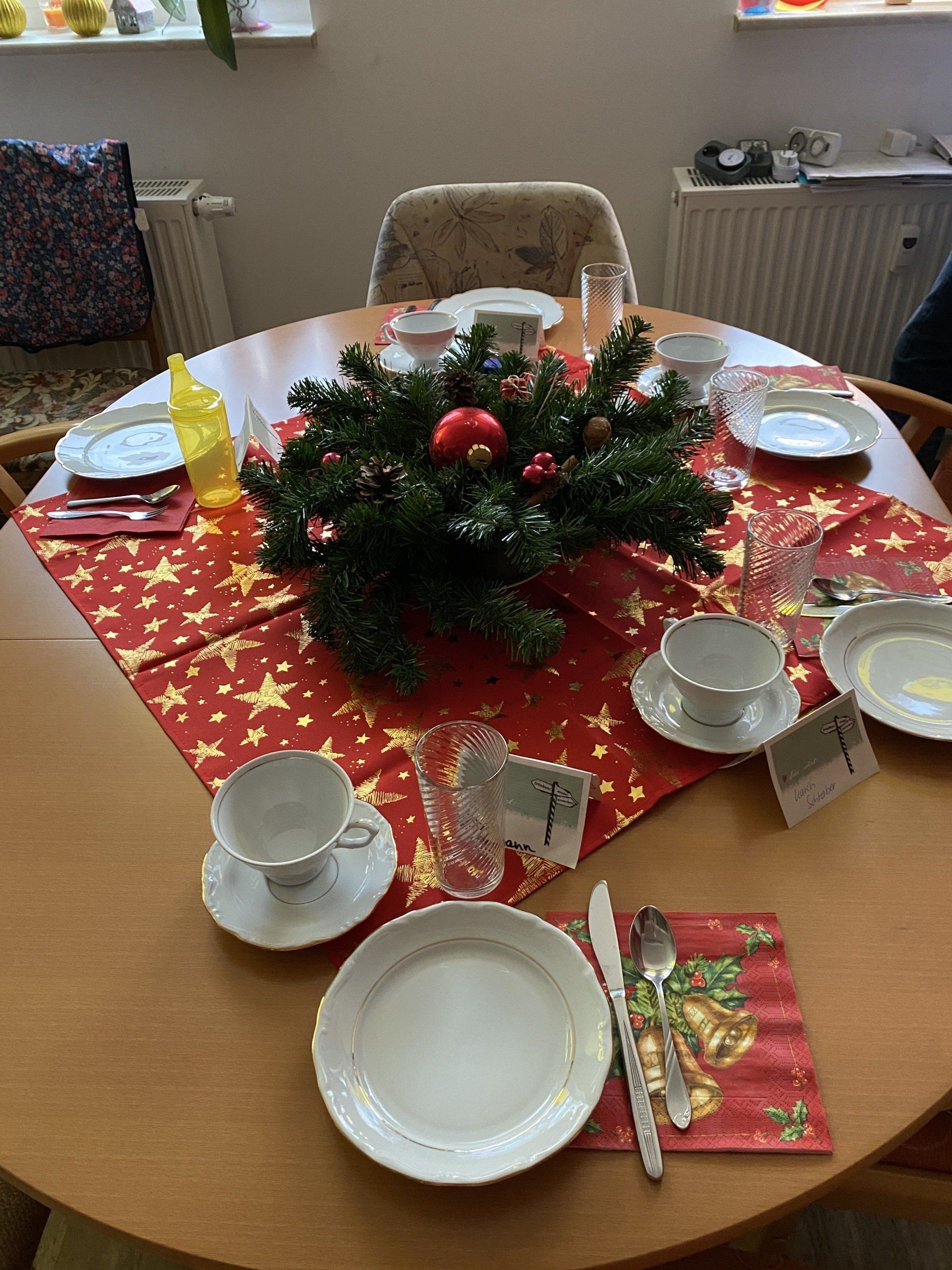 Runder Tisch für ein Essen mit roter Tischdecke mit Sternenmuster und Weihnachtsdekoration. 