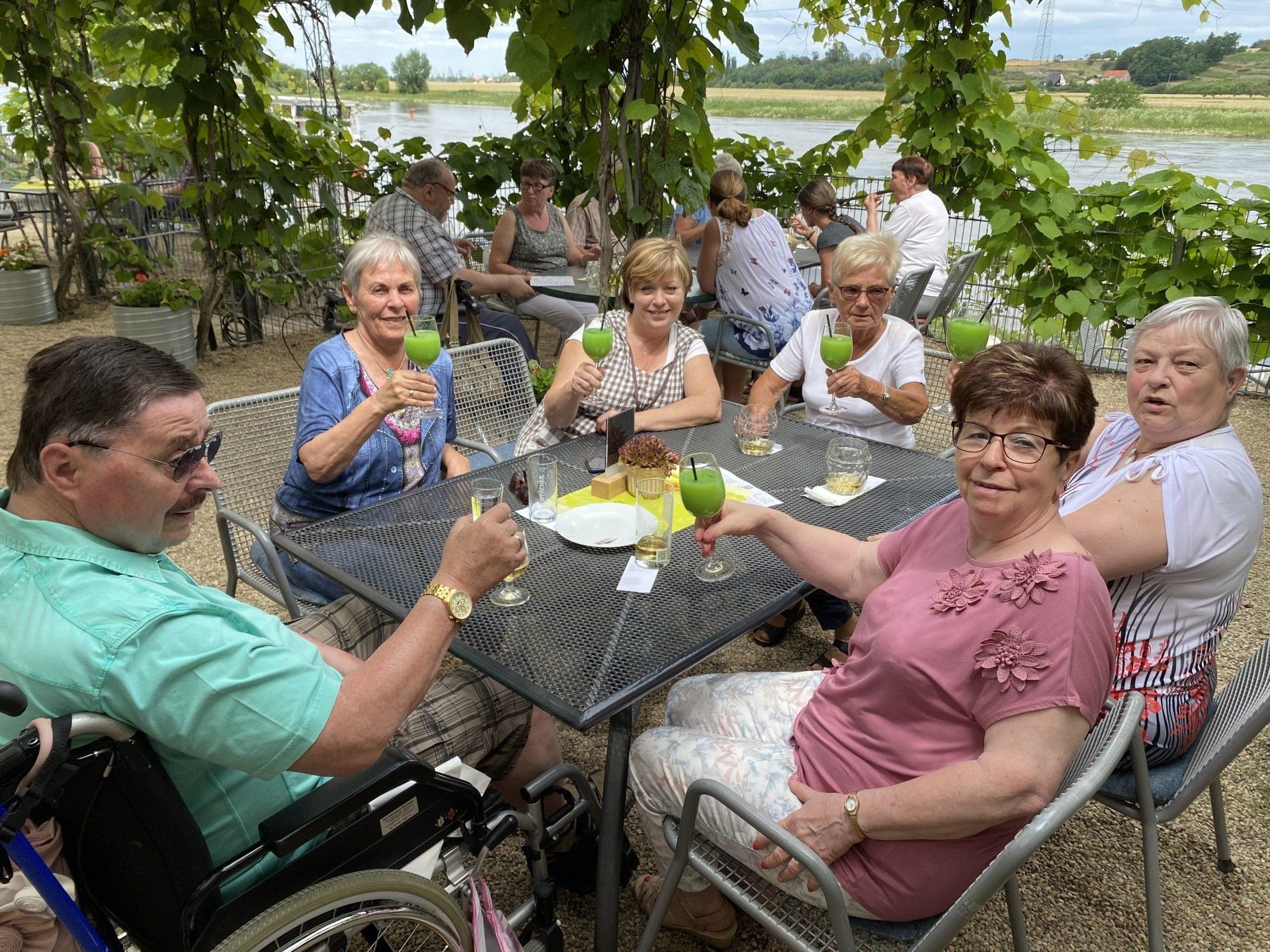 Eine Gruppe von Menschen stößt im Freien an einem Fluss mit grünen Äpfeln an.