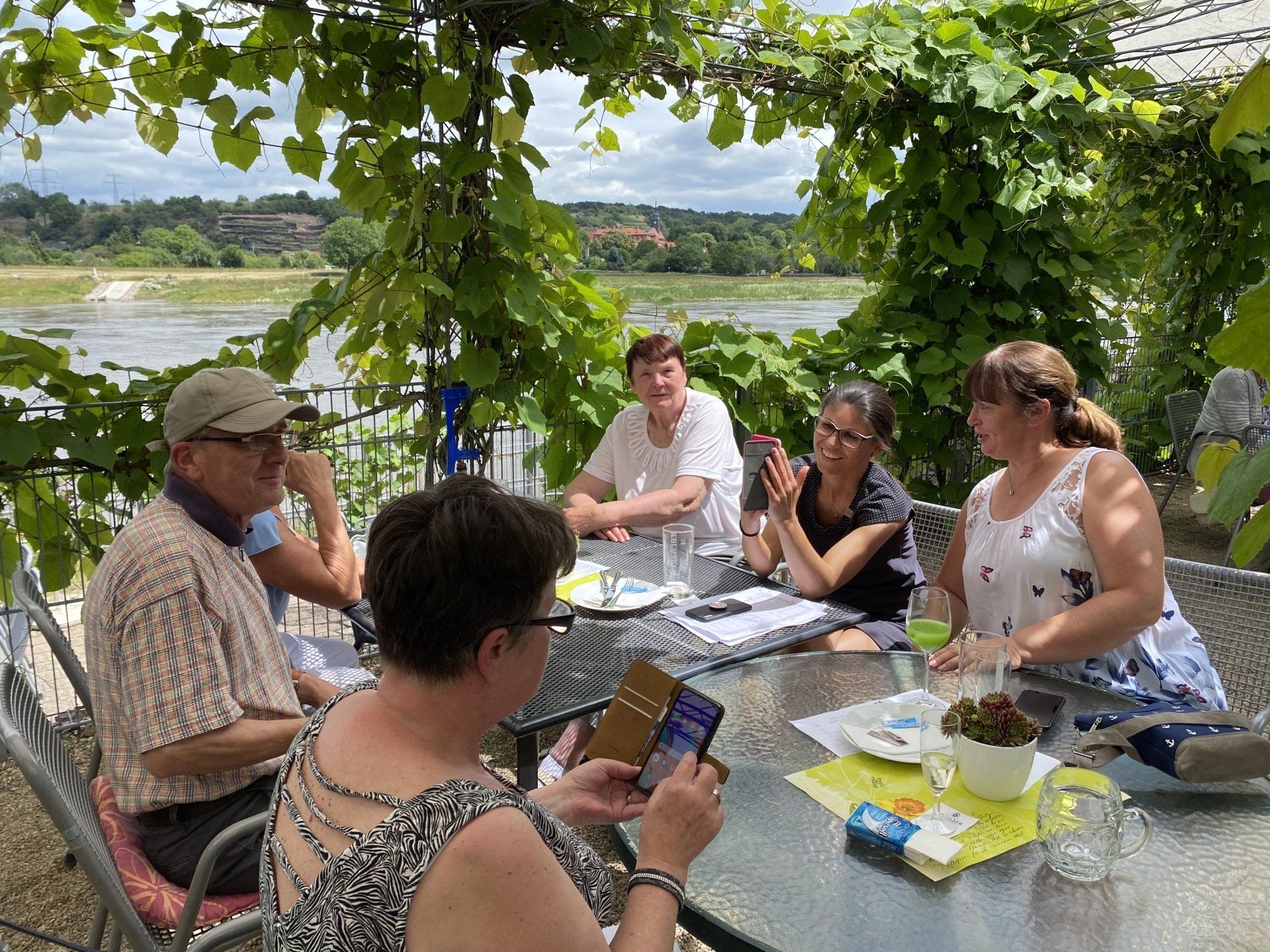 Eine Gruppe von Menschen unterhält sich an einem Tisch im Freien unter Weinreben 