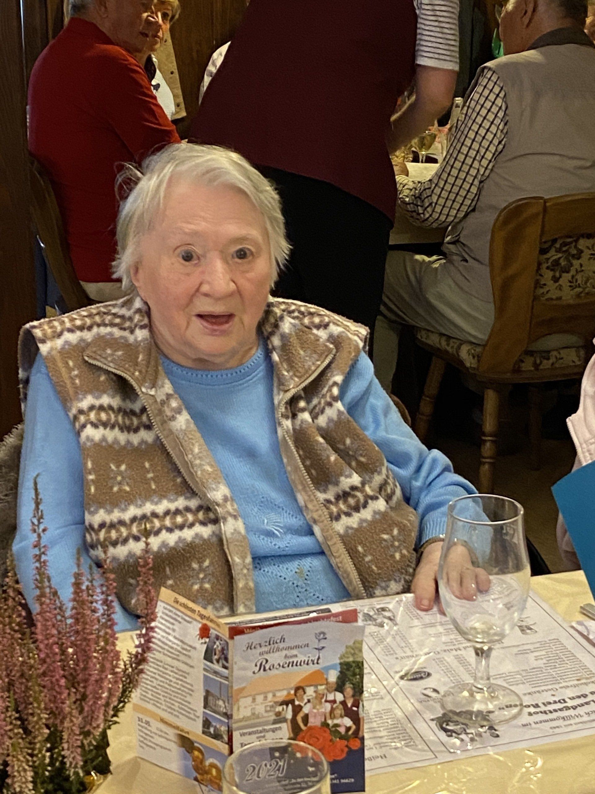 Eine ältere Person sitzt in einer Strickweste an einem Tisch in einem Restaurant.