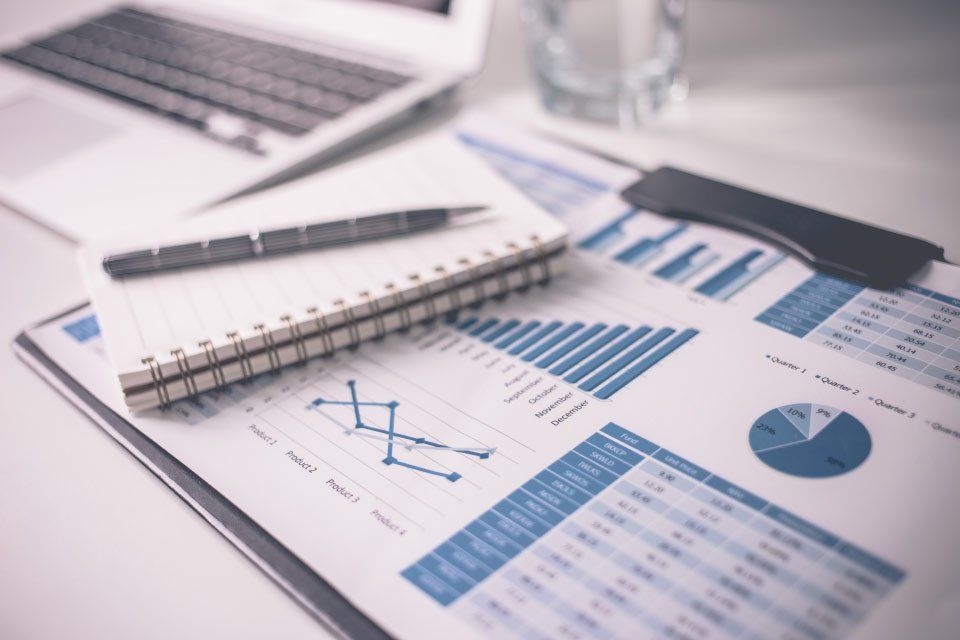 Computer portatile, blocco note, penna e grafici finanziari su una scrivania.