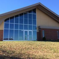 Modern building with glass front, brick base, tan siding on grassy hill.