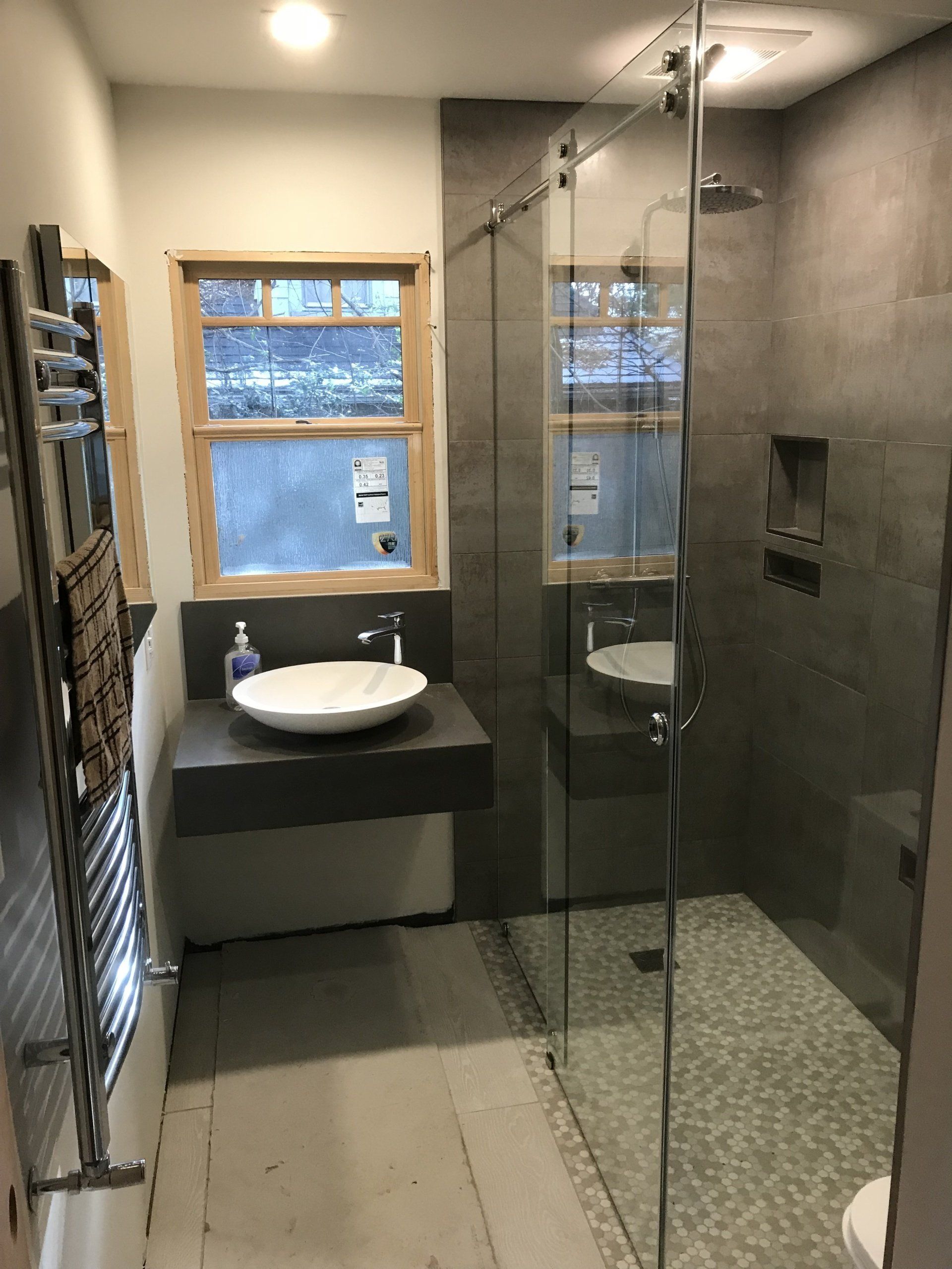 Modern bathroom with custom frameless glass shower enclosure, natural wood window frame, and large gray tile walls.