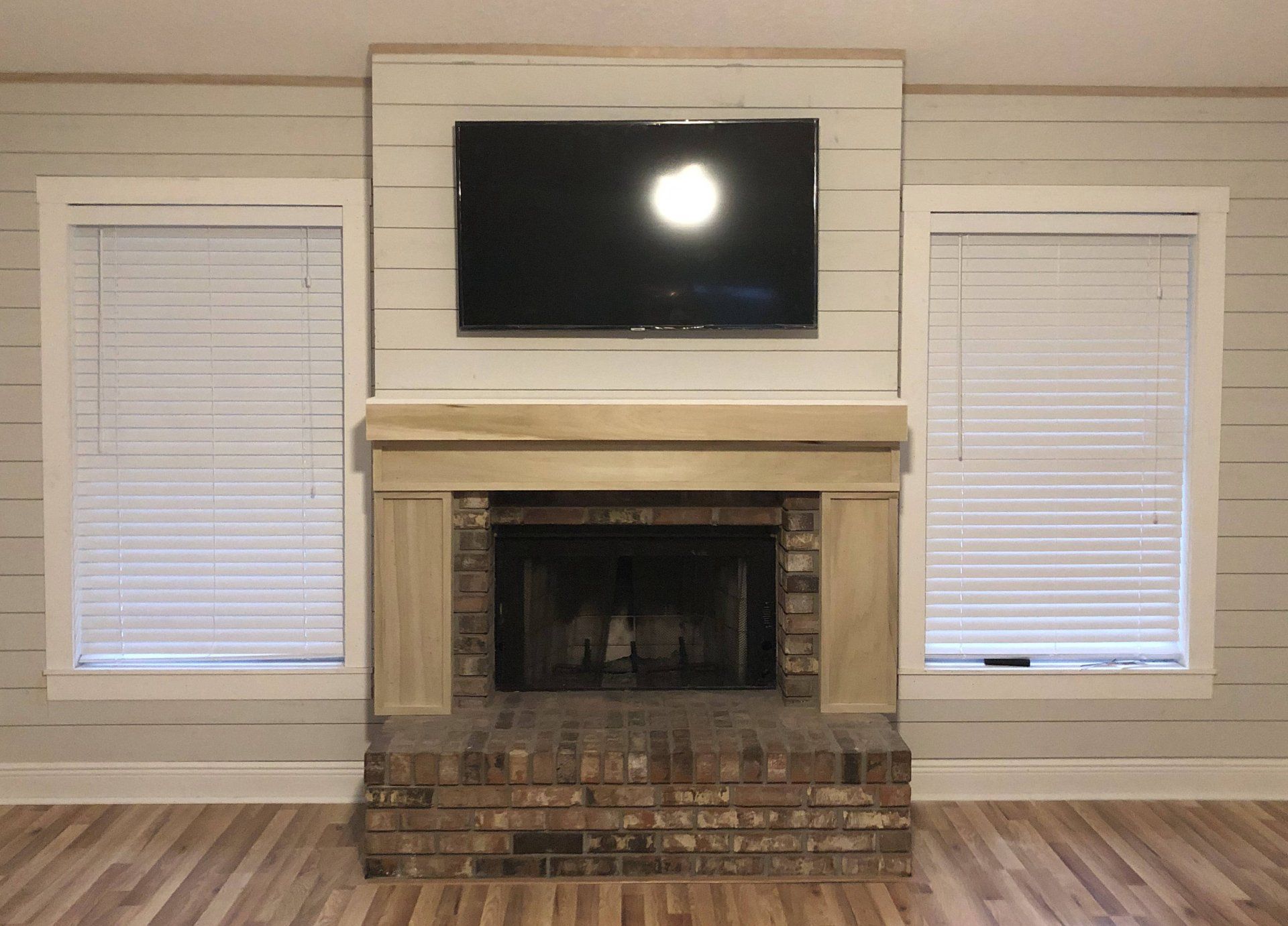 Fireplace with mounted TV, flanked by windows with blinds, set in a light gray wall.
