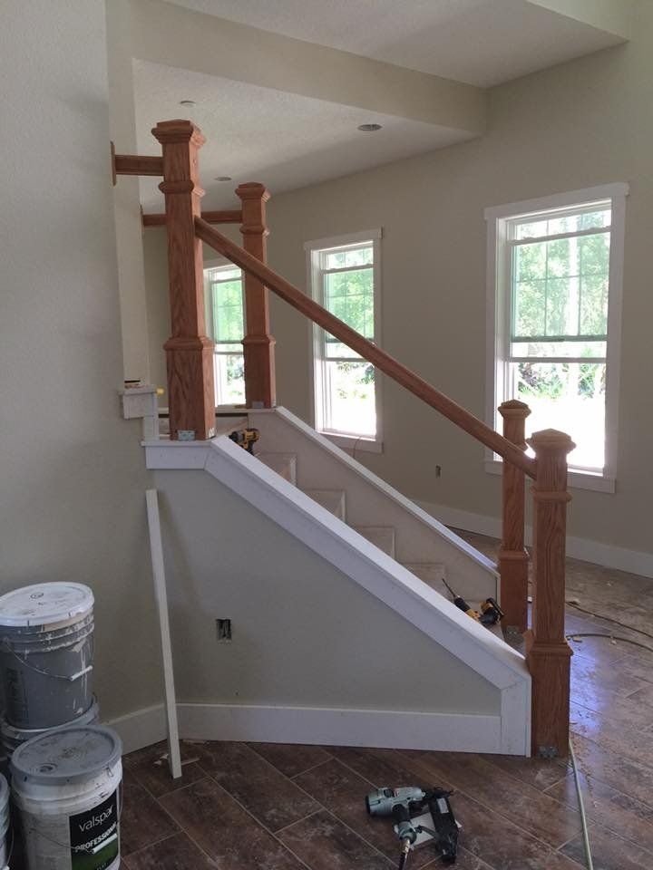 Staircase with wooden railing and posts; newly constructed interior. Paint buckets and tools are in the foreground.