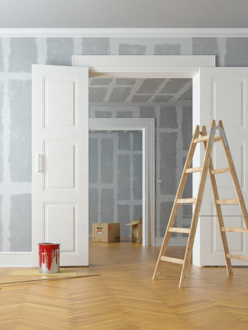 Interior renovation with open doorway, ladder, paint can, and unfinished walls.