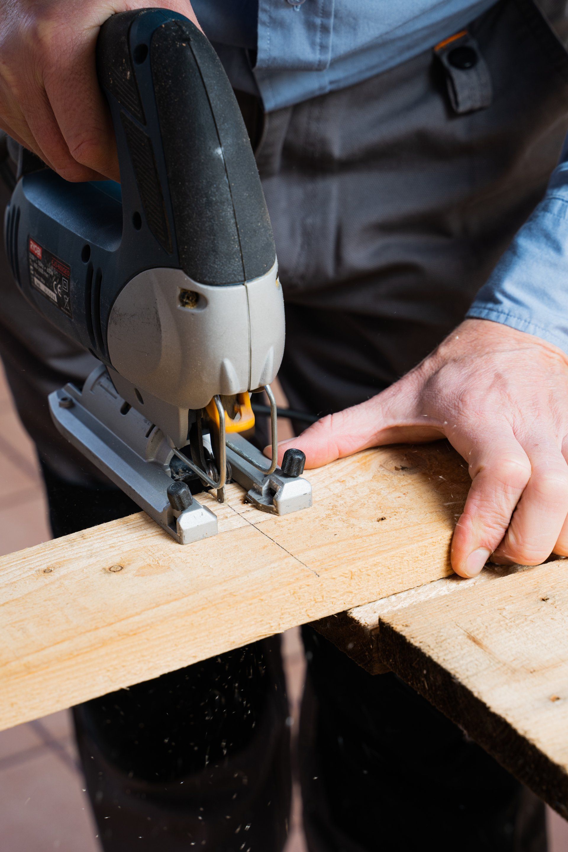 Person uses a jigsaw to cut a wooden board on a work surface.