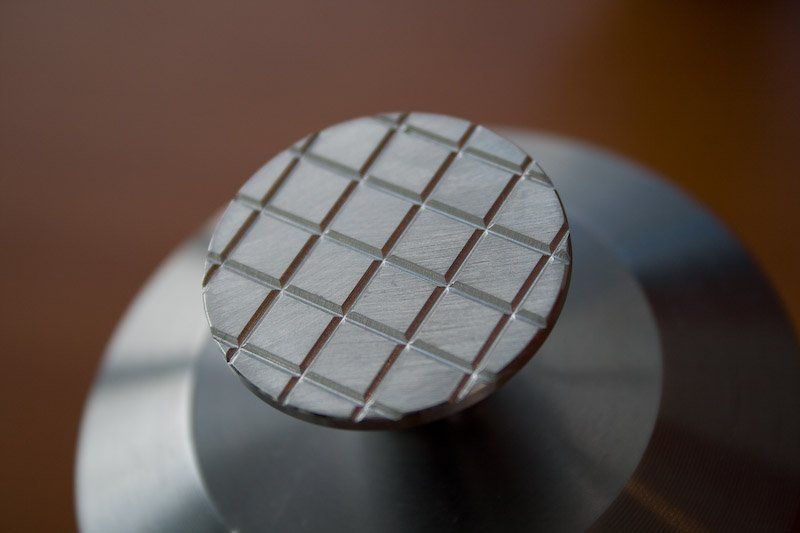 Nahaufnahme eines Metallknopfes mit Gittermuster auf einem größeren, gestuften Metallsockel.