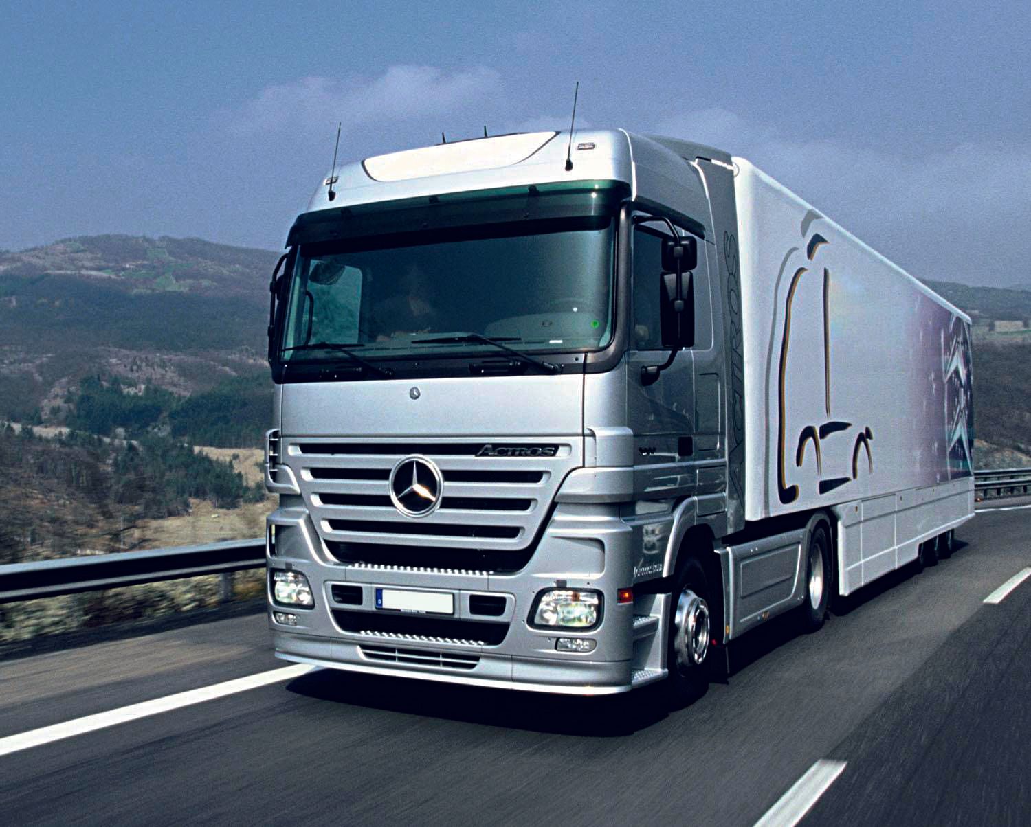 Ein silberner Mercedes-Sattelzug mit weißem Anhänger auf der Autobahn. Strahlender Sonnenschein, im Hintergrund grüne Hügel.