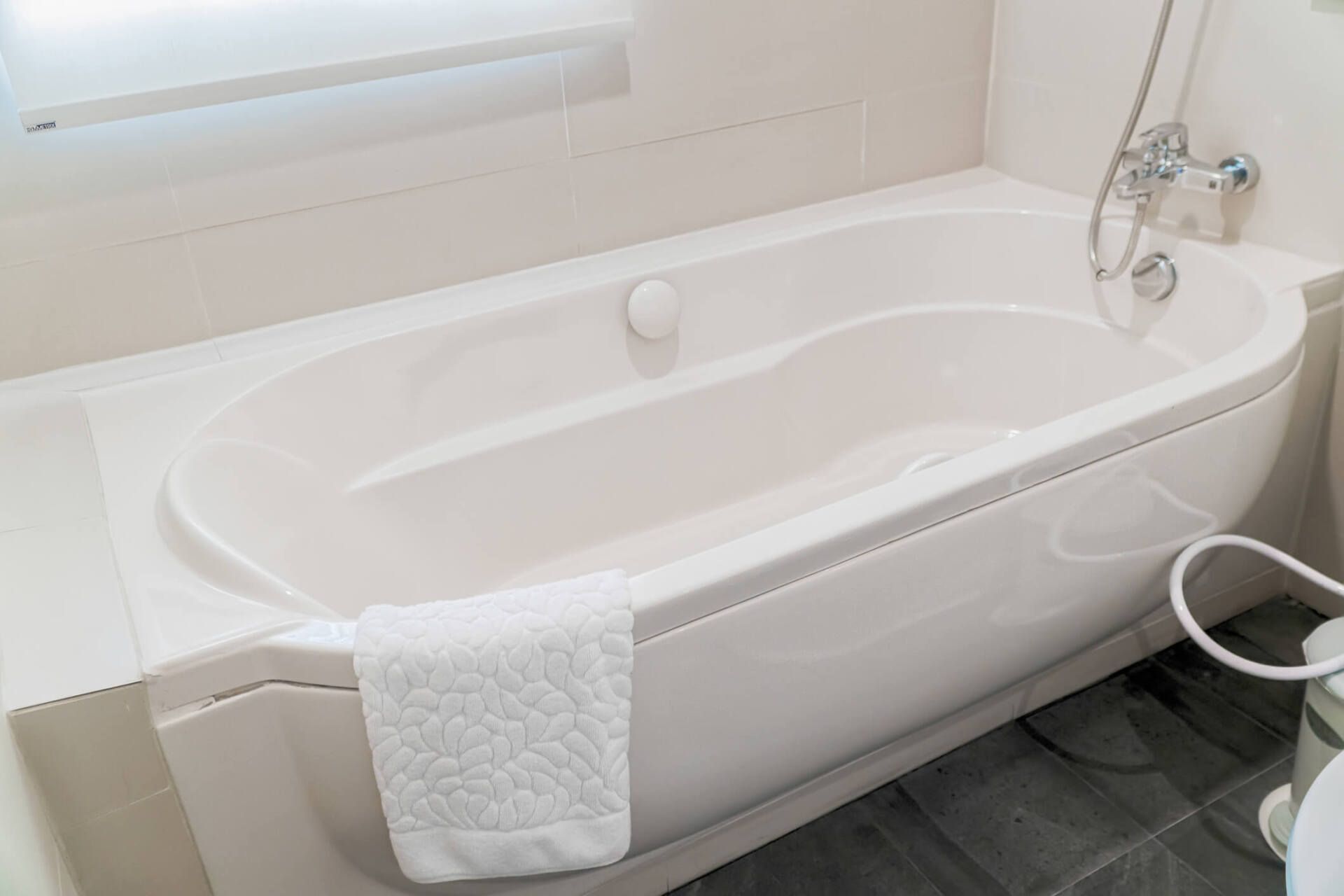 White bathtub in a bright bathroom with a towel draped over the side and shower fixtures nearby