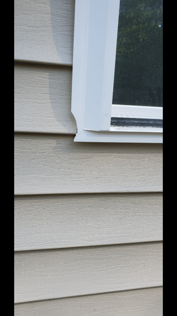 Close-up of beige house siding beside a white-trimmed window with dark glass.