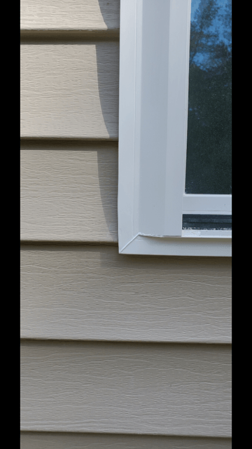 Close-up of a white-framed window on beige siding with a small crack at the lower corner.