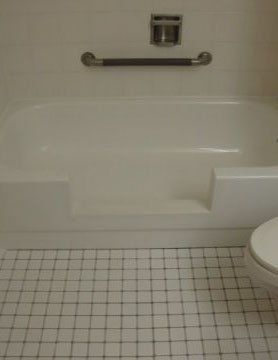 Accessible bathtub with grab bar, built-in seat, tiled floor, and toilet nearby