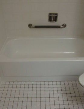 White bathtub with grab bar and shower fixture in a tiled bathroom.