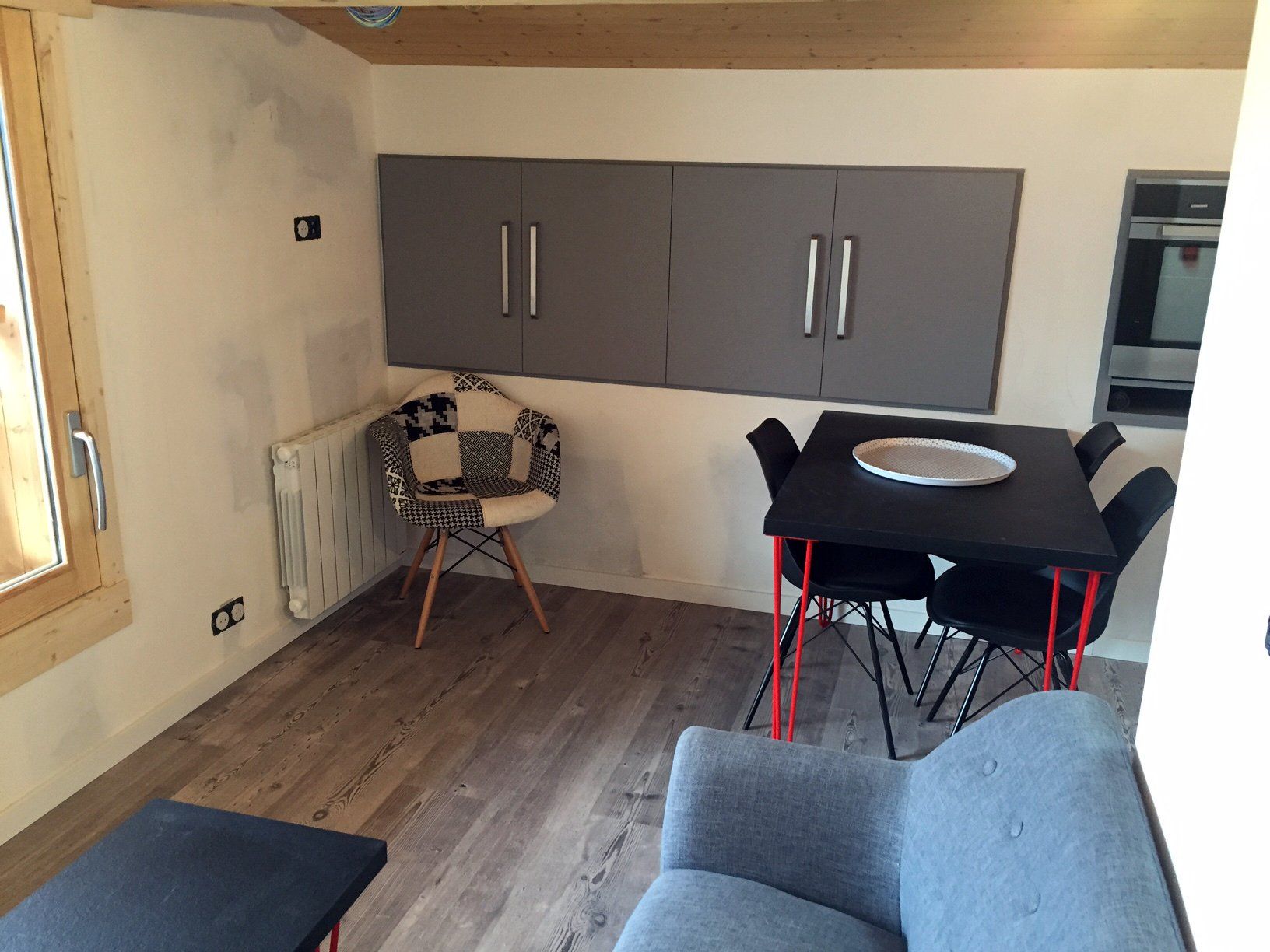 Petite chambre meublée avec des armoires grises, une table et des chaises, un radiateur et un canapé bleu.