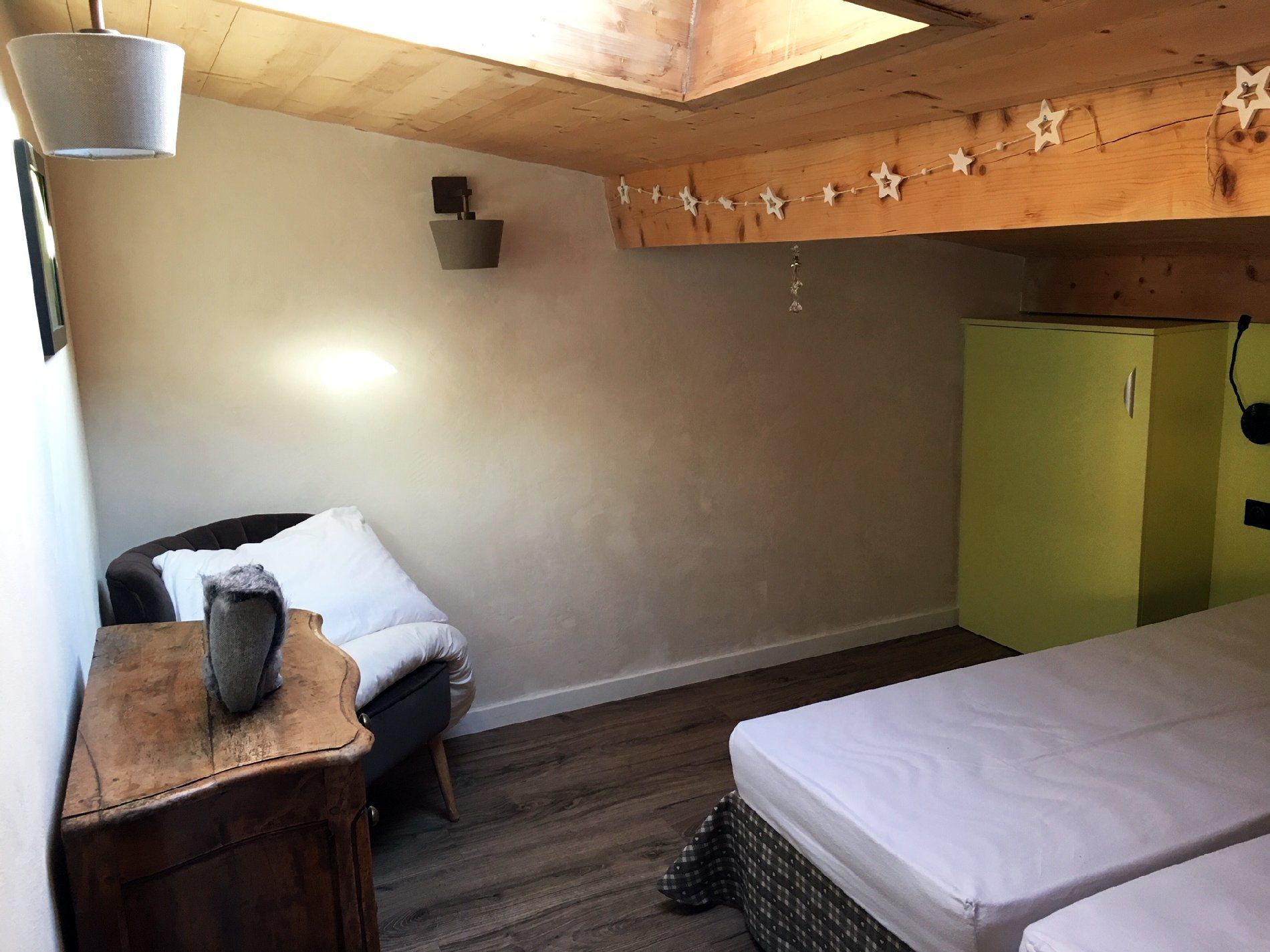 Petite chambre avec deux lits, un plafond en bois et une banquette près de la fenêtre, le long du mur.