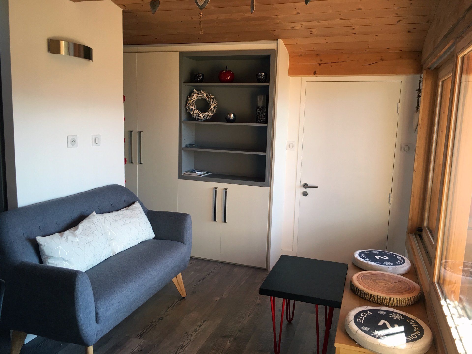 Salon confortable avec canapé bleu, étagères noires, petite table et grandes fenêtres à côté d'une porte blanche