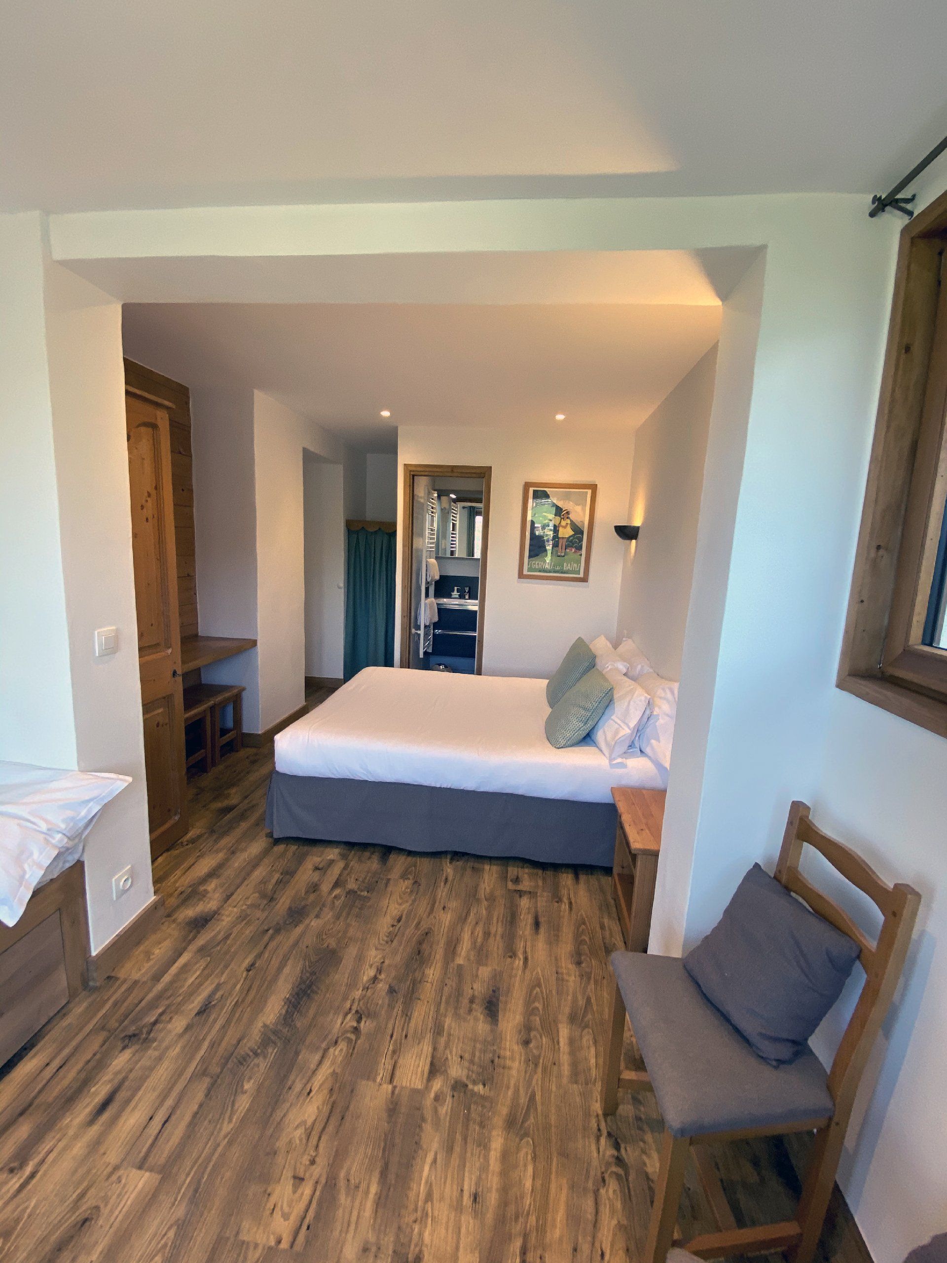 Chambre moderne avec parquet, lit, banc, coin bureau et œuvres d'art murales visibles à travers une large porte.