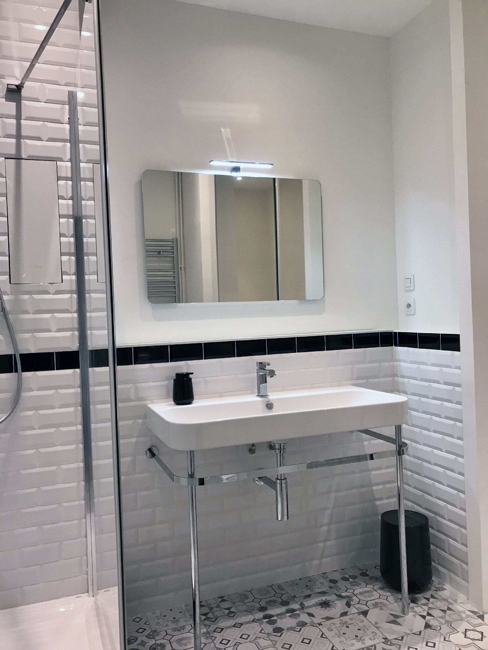 Petite salle de bains carrelée de blanc avec lavabo, miroir, applique murale et espace douche.