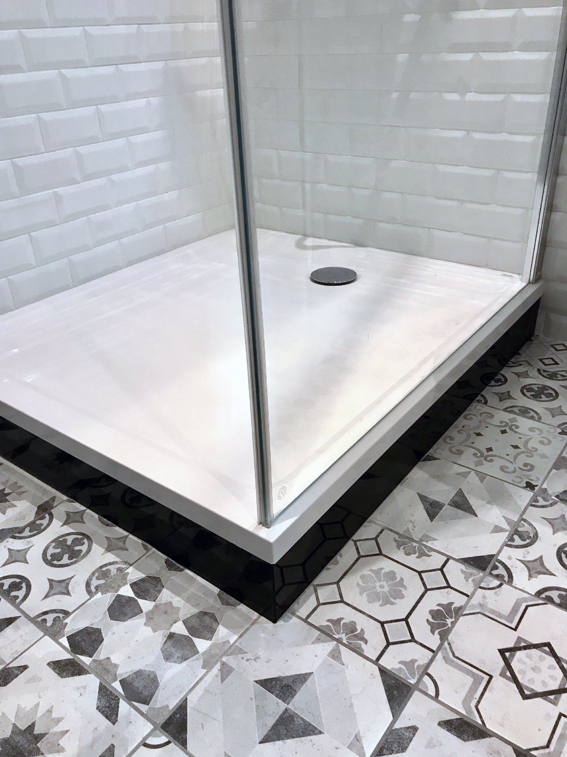 Cabine de douche en verre avec murs carrelés de blanc et carrelage au sol à motifs