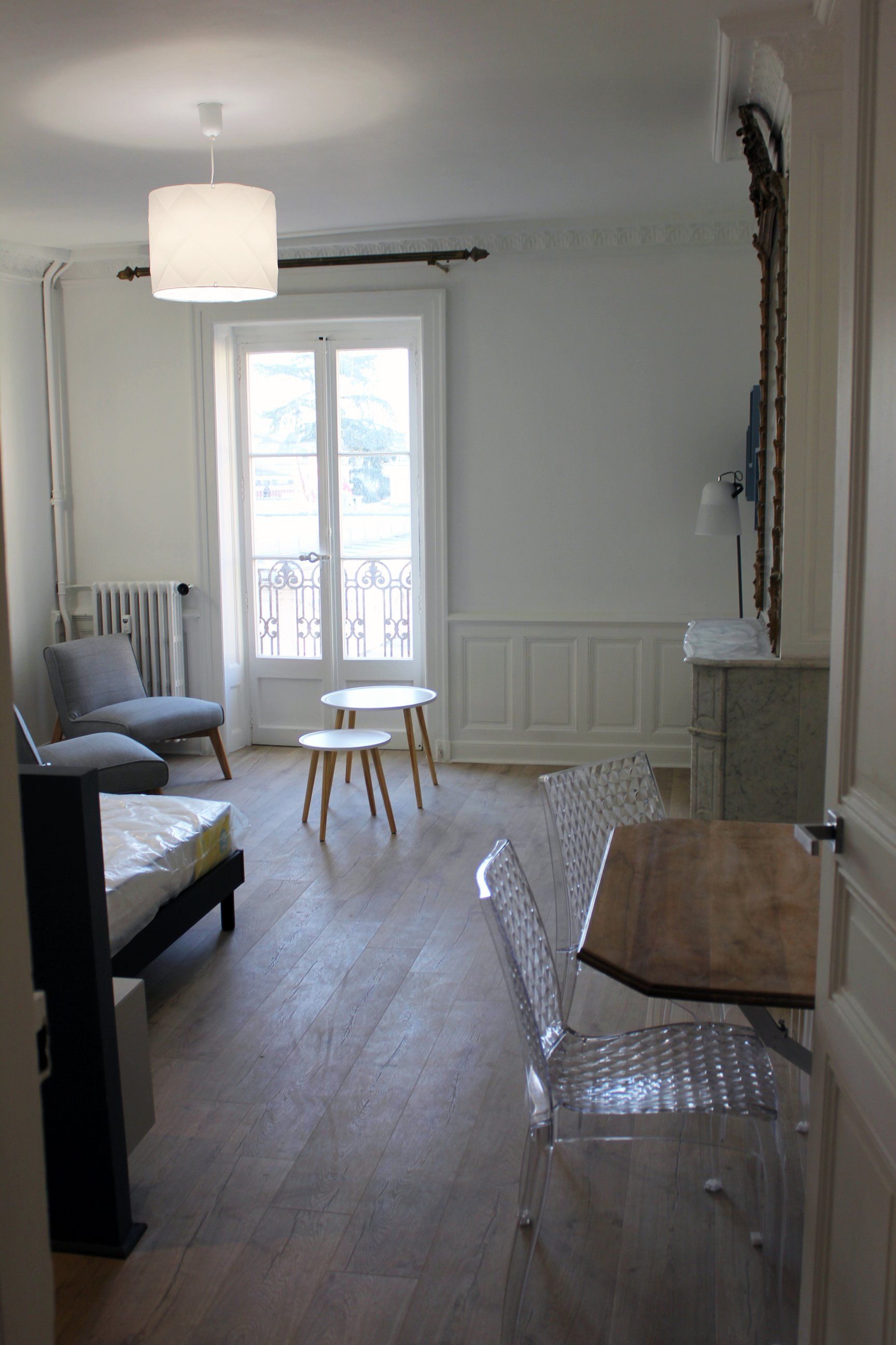Salon minimaliste et lumineux avec canapé gris, petite table, porte blanche et suspension lumineuse.