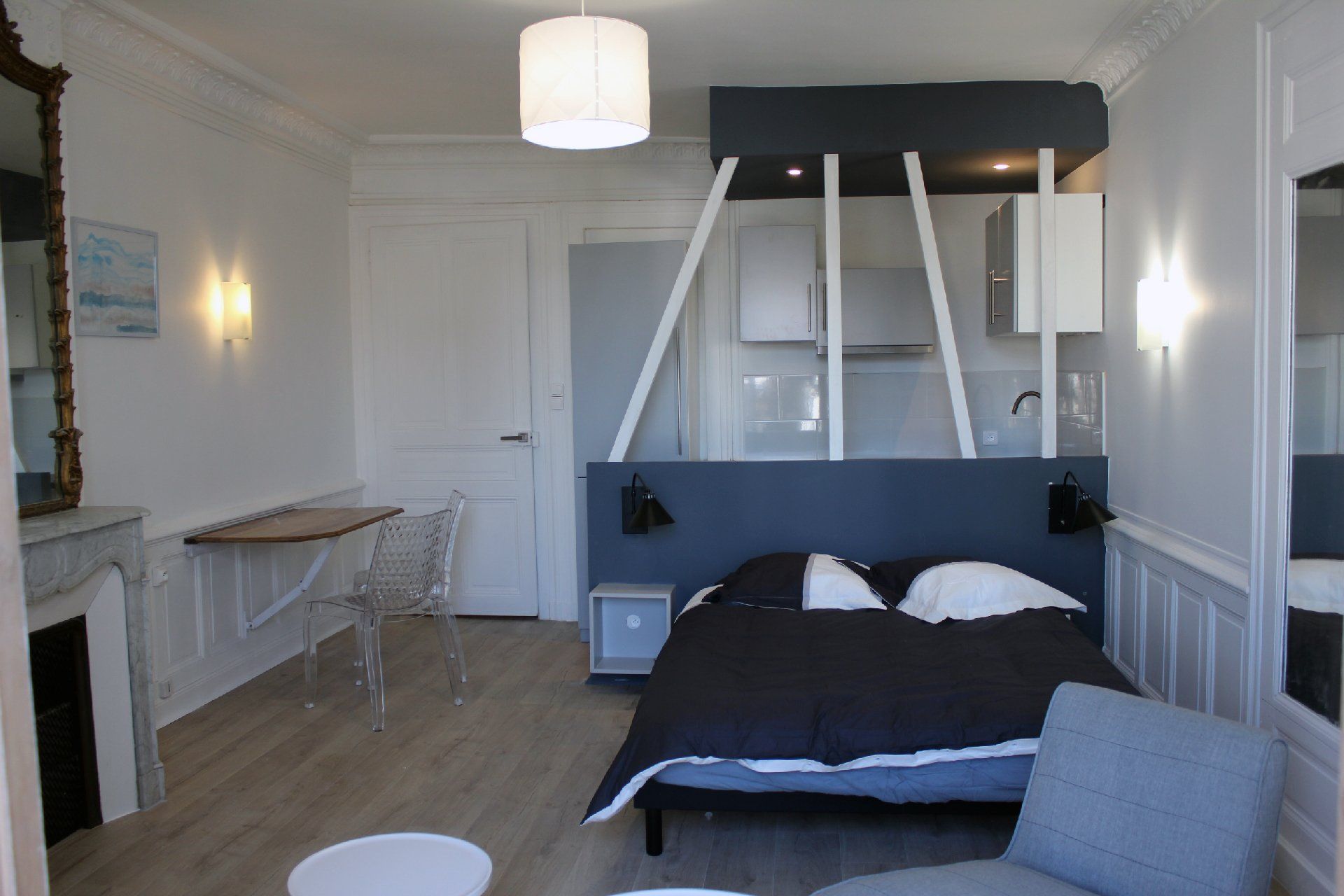 Chambre moderne et lumineuse avec lit noir et blanc, cheminée et grands volets.
