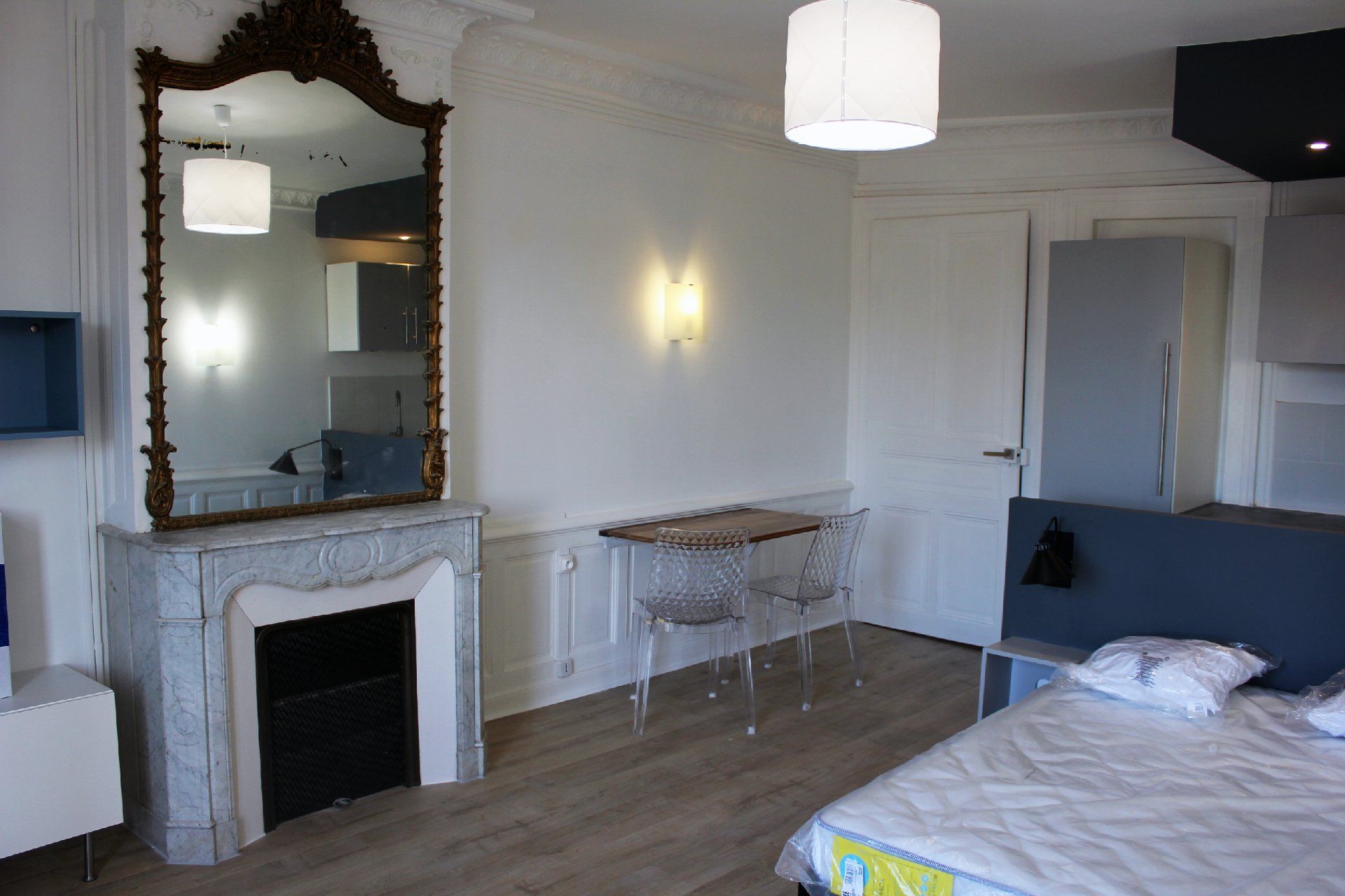 Chambre lumineuse avec cheminée, miroir orné, murs blancs et lit dans un coin