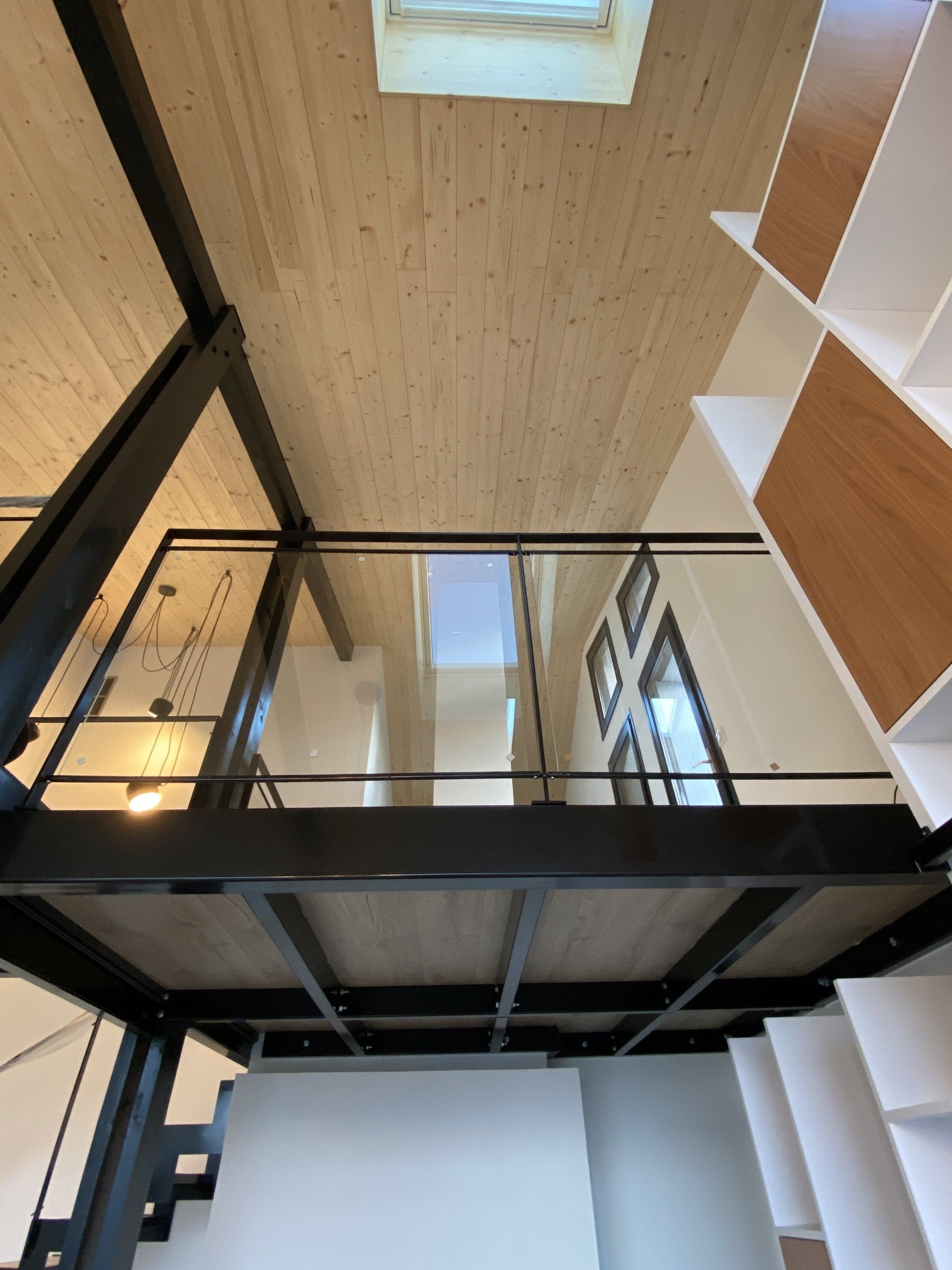 Intérieur de loft moderne avec mezzanine à balustrade en verre, poutres en acier noir, plafond en bois et puits de lumière