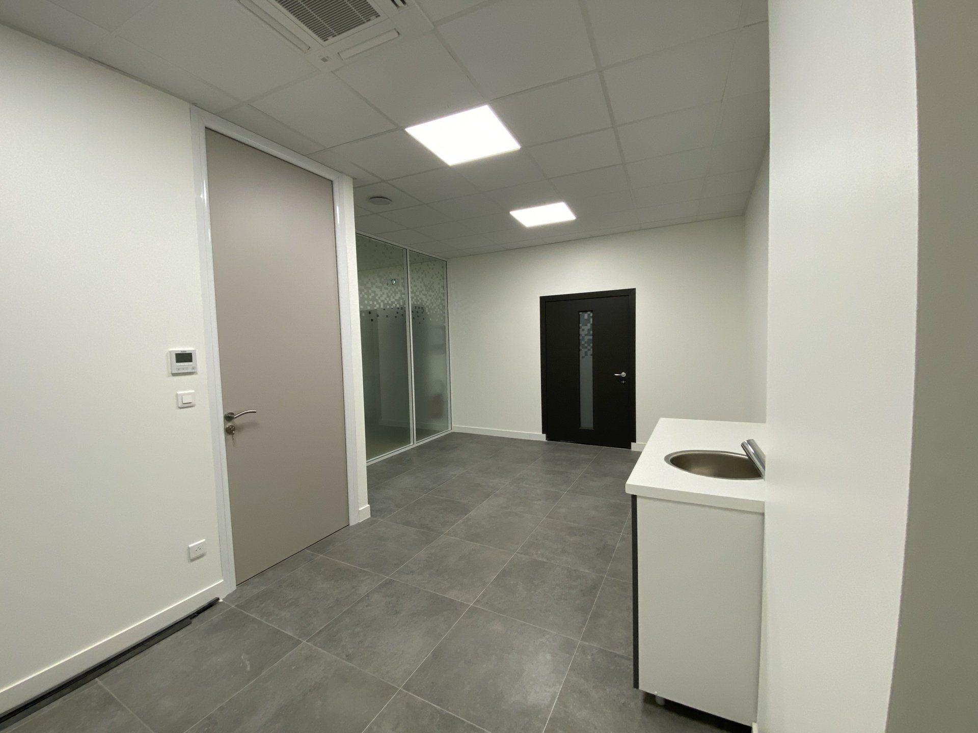 Couloir moderne vide avec murs blancs, sol carrelé gris et une armoire noire près d'un petit comptoir