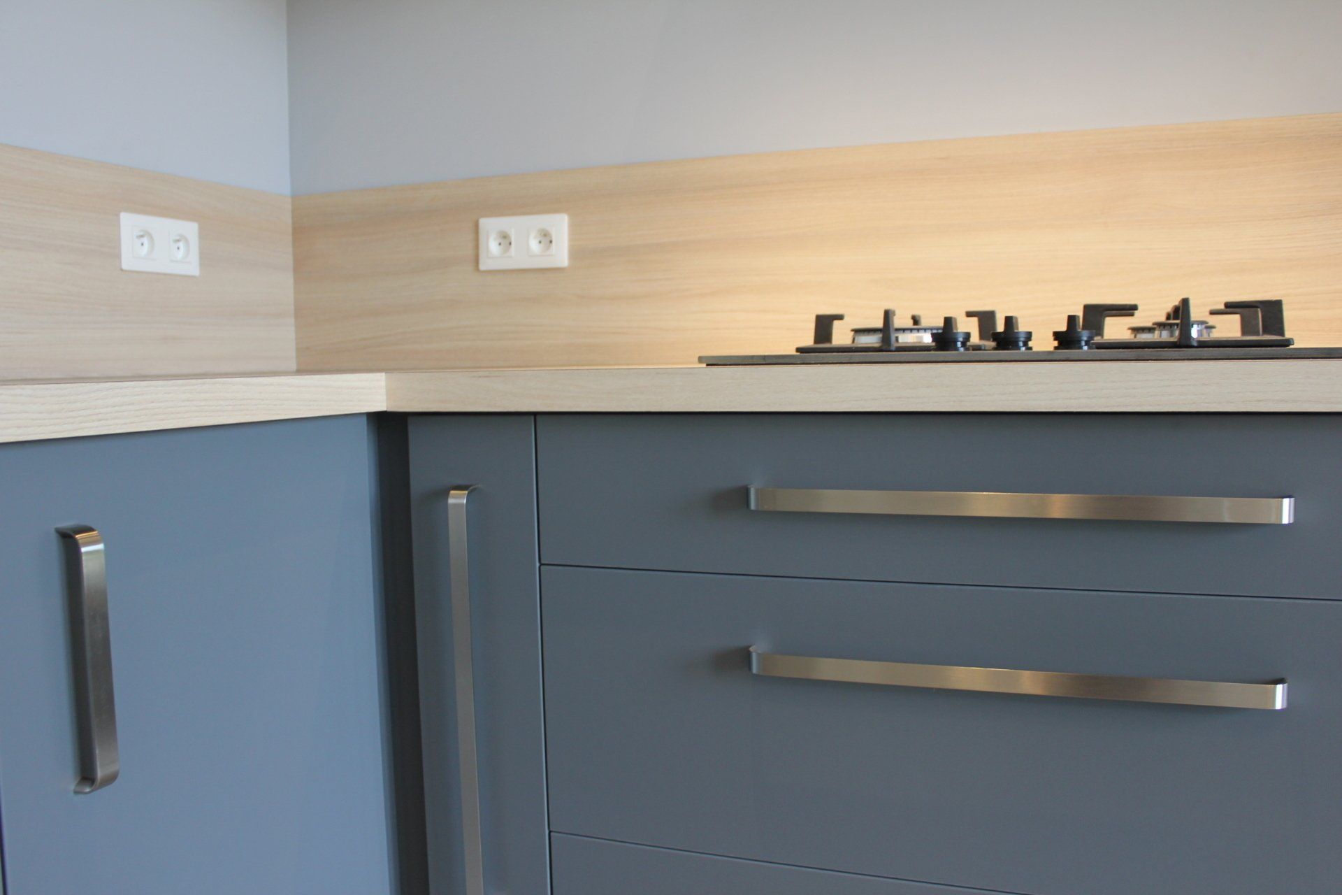 Comptoir de cuisine moderne avec armoires bleues, crédence en bois et plaque de cuisson à gaz noire