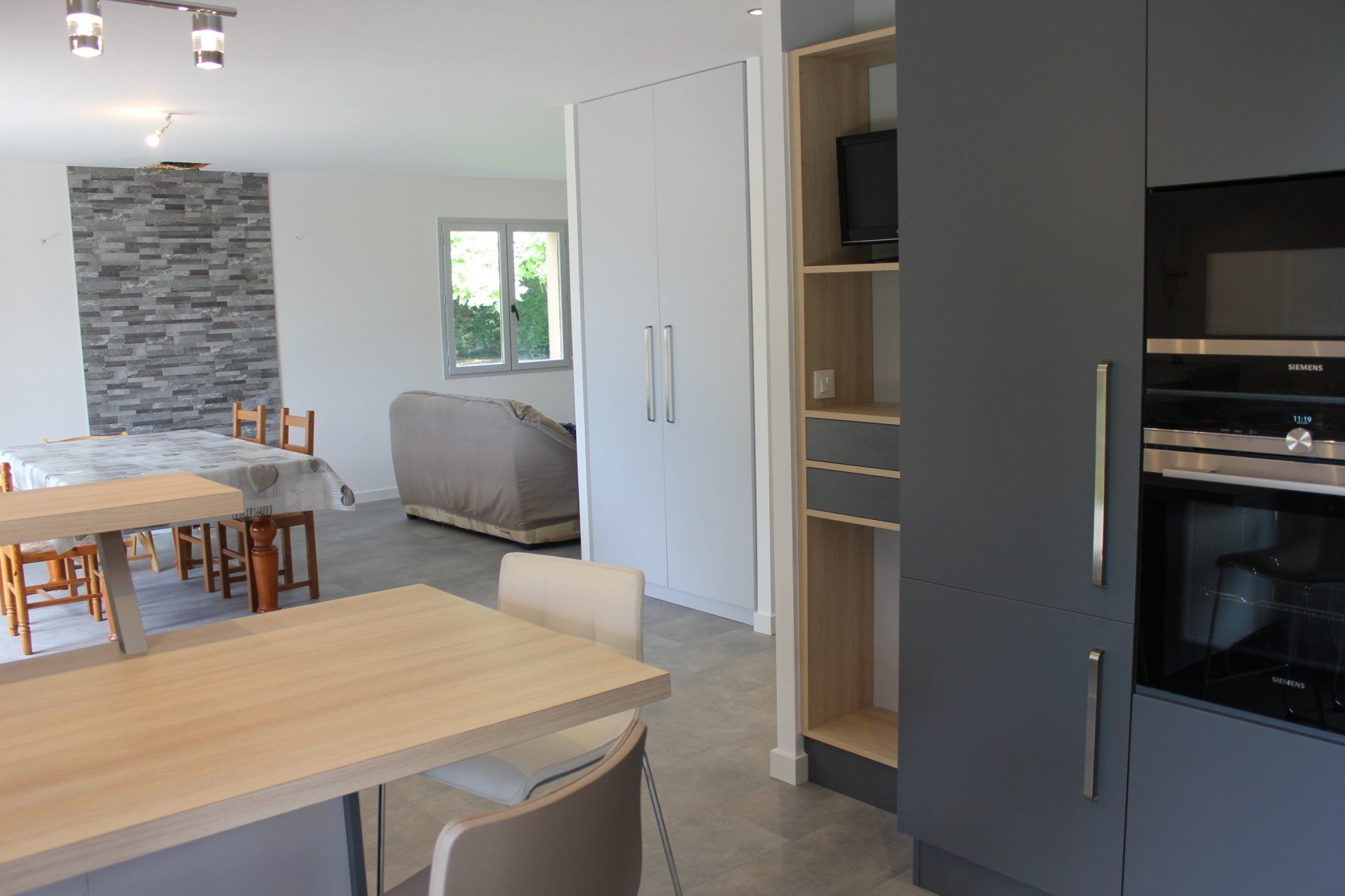 Cuisine et salle à manger modernes avec table, chaises, placards gris et porte de garde-manger ouverte