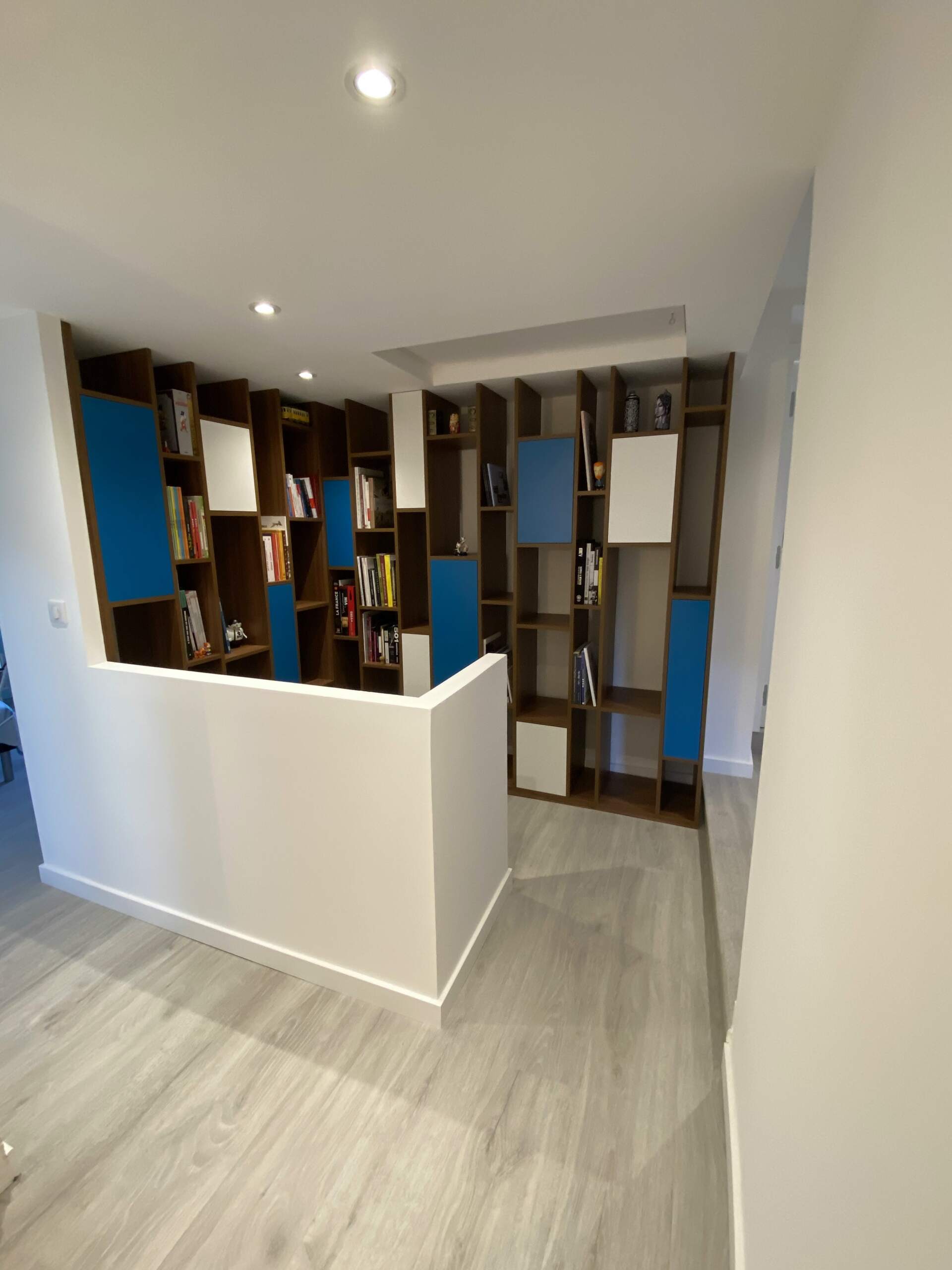 Pièce moderne vide avec parquet clair, muret blanc et étagères intégrées dans des tons bleus et bois foncé.