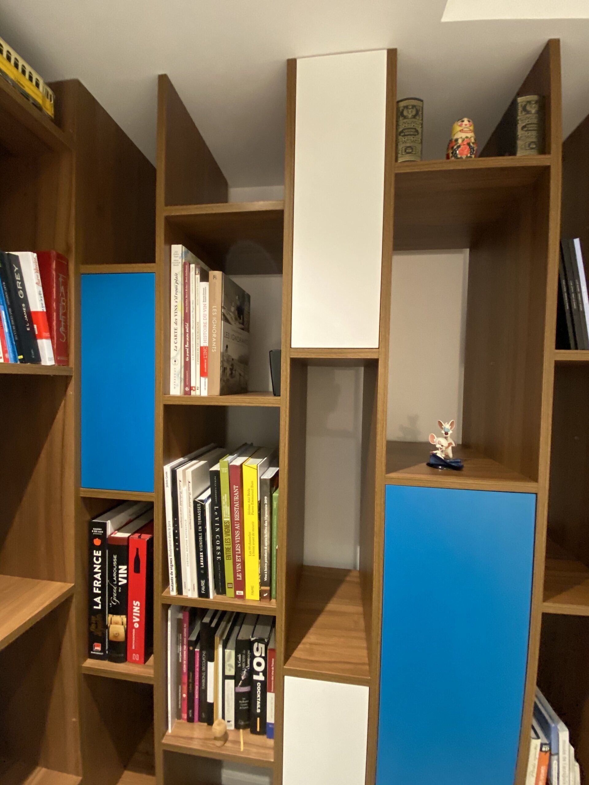 Des étagères en bois avec des livres et des panneaux de rangement bleus entourent une niche centrale blanche.
